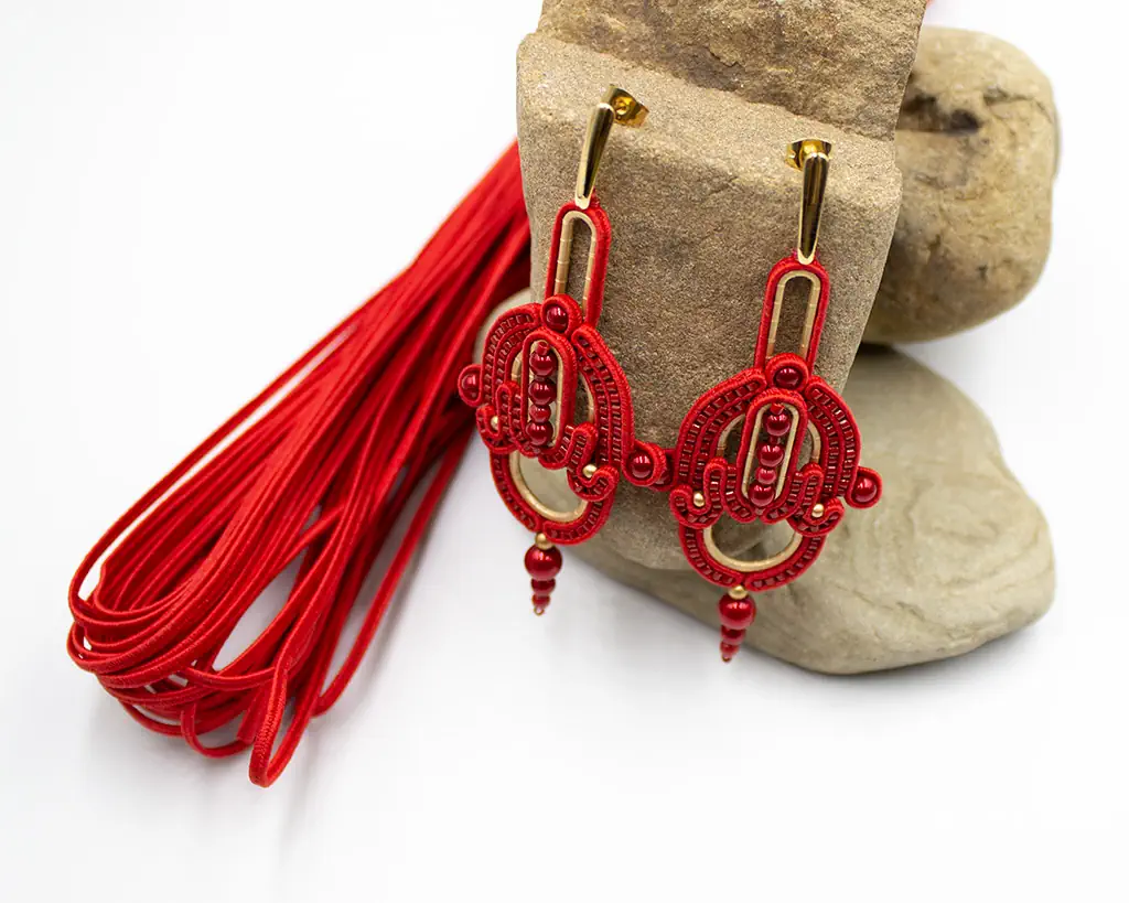 Czerwone ażurowe kolczyki o eleganckim fasonie. Doskonały dodatek do klasycznych stylizacji. Czerwone pasma sutaszu przeplatają się z czerwienią pereł Preciosa oraz subtelnym jasnym złotem.